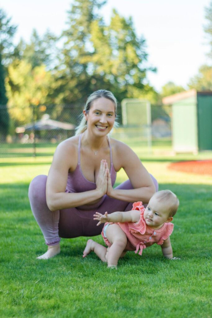 A mother and her baby enjoying yoga outside in a park on a sunny day.